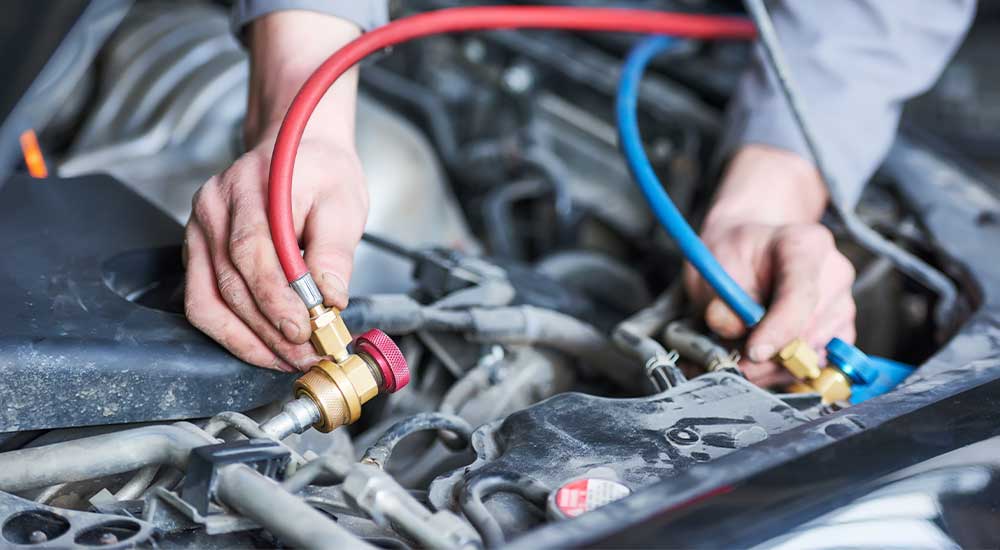 A closeup picture of a mechanic’s hands as they regas a vehicle’s air conditioning system.