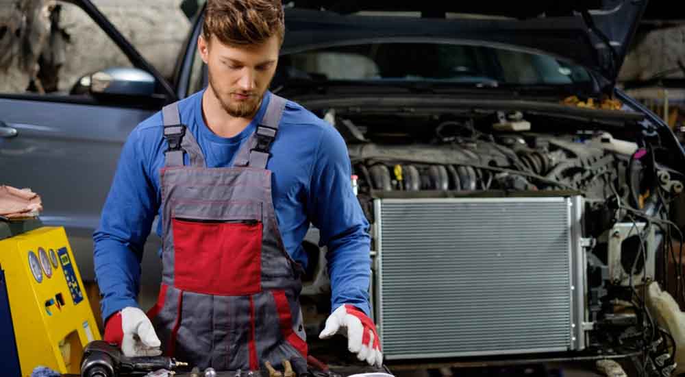 Mechanic inspecting car radiator for EV battery thermal management and cooling system service.