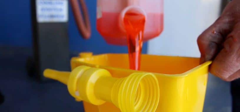 A Natrad mechanic pours red coolant concentrate into a large specialised radiator funnel, which is fitted into a car radiator.