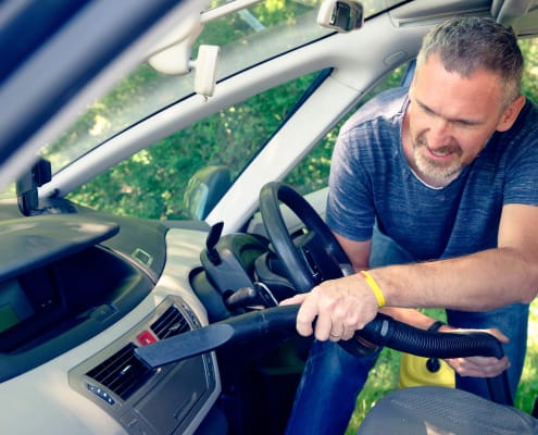 Man hoovering air vent in car