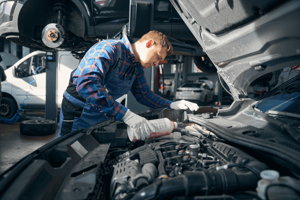 Mechanic pouring coolant into a car’s cooling system while performing maintenance under the bonnet in a professional auto repair workshop.