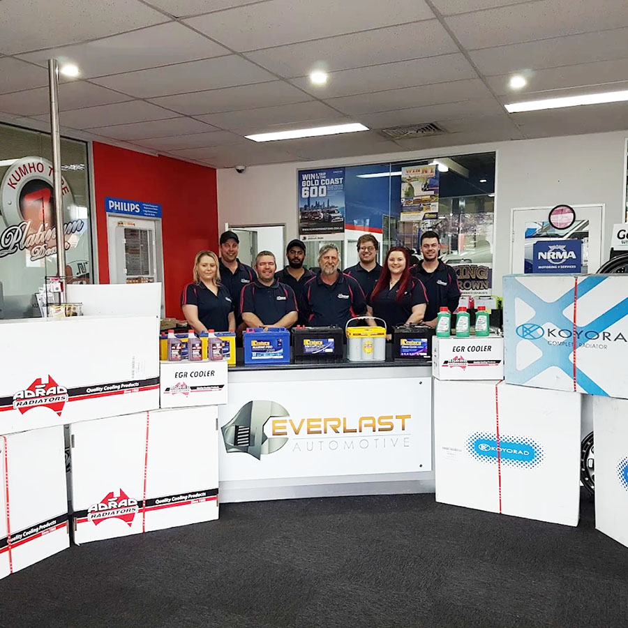 The team stands behind a counter surrounded by stacked Natrad radiator boxes and car batteries.